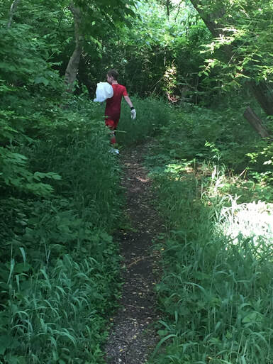 Picture: A boy in a red shirt walking on a path in the woods with a garbage bag. 